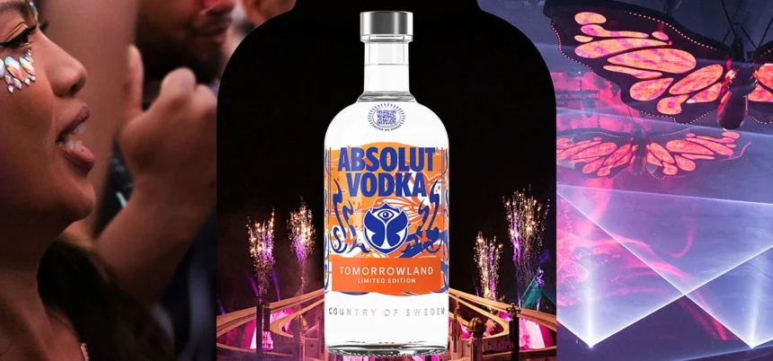 Botella de Absolut Vodka edición limitada Tomorrowland 2025 rodeada de elementos visuales del festival como luces, fuegos artificiales y una mariposa luminosa.