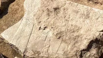 Piedra tallada con relieves antiguos parcialmente erosionados, hallada en una excavación arqueológica de una estructura oculta por 2700 años.