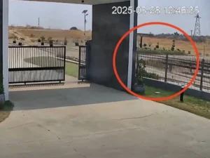Entrada de un complejo residencial con portón metálico abierto y una grieta visible en el pavimento de concreto.