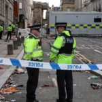 Policías británicos custodian una zona acordonada en una calle llena de escombros tras un atropello masivo en Liverpool.