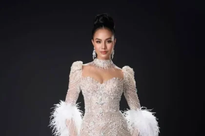 Opal Suchata Chuangsri, Miss Mundo 2025, posando con un elegante vestido de gala bordado en pedrería y detalles de plumas blancas, frente a un fondo oscuro.