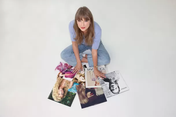 Taylor Swift sentada en el suelo rodeada de portadas de sus primeros seis discos recuperados, simbolizando su victoria artística en 2025.