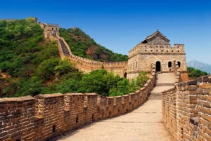Vista panorámica de la Gran Muralla China serpenteando sobre colinas verdes bajo un cielo despejado.