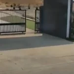 Entrada de un complejo residencial con portón metálico abierto y una grieta visible en el pavimento de concreto.