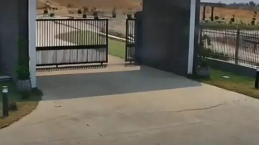 Entrada de un complejo residencial con portón metálico abierto y una grieta visible en el pavimento de concreto.