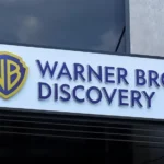 Logo de Warner Bros. Discovery en la fachada de un edificio corporativo, con el escudo WB en amarillo y azul.